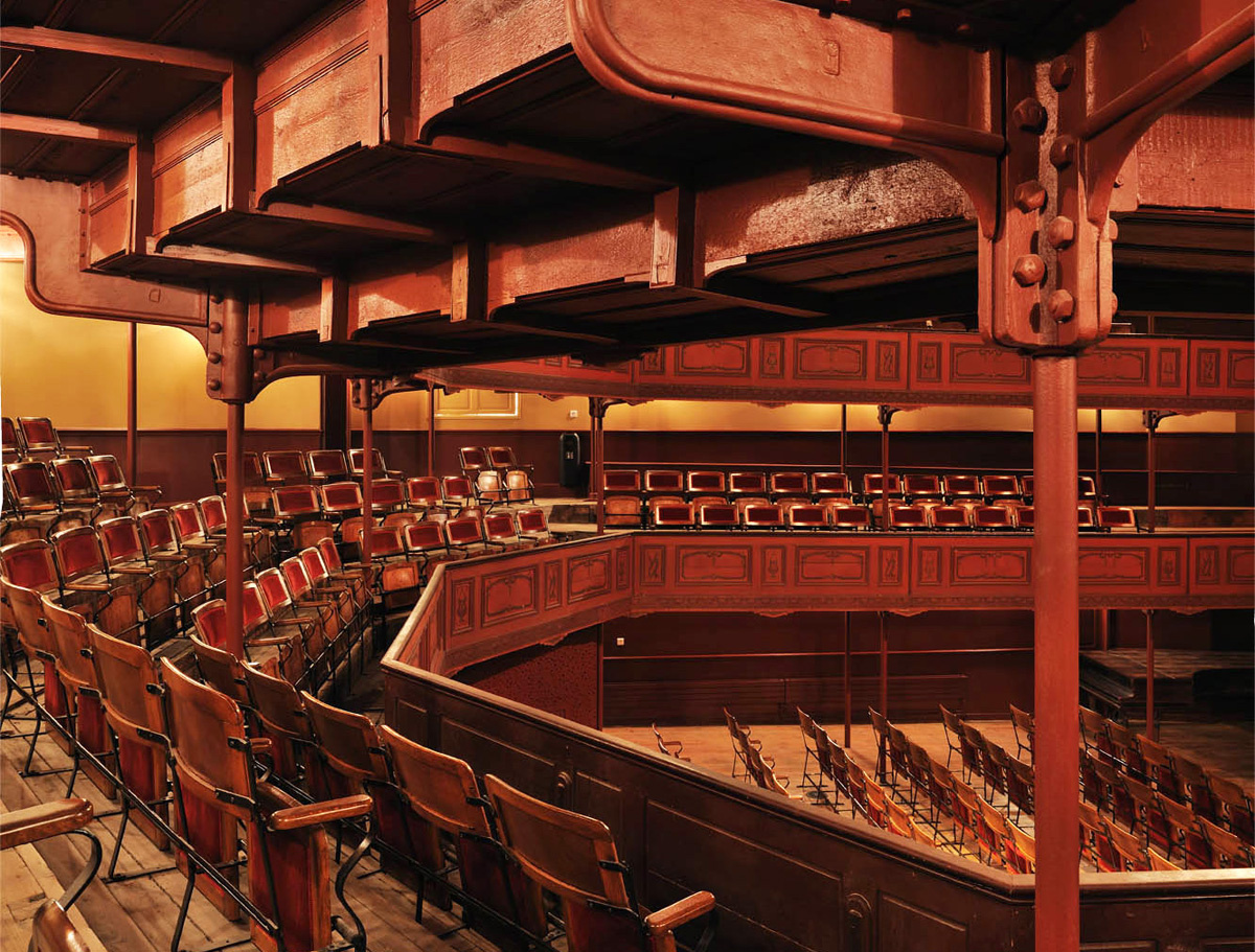 Le premier balcon du théâtre du Familistère, ses sièges en bois et tissu rouge.