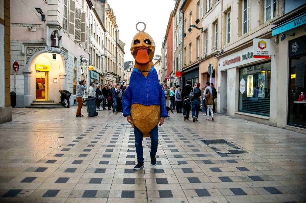 Un homme en costume de canard au milieu d'une rue pietonne cmmecrçante.