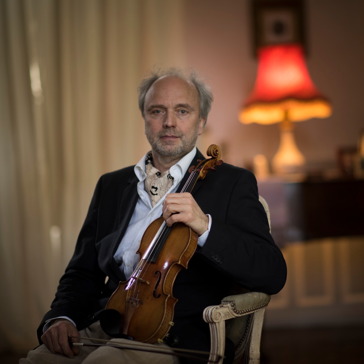 Un homme assis dans un salon, un violon à la main.