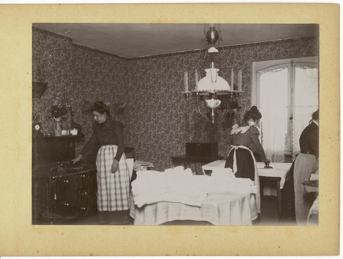 La photographie montre une scène de repassage dans la cuisine d'un logement du F