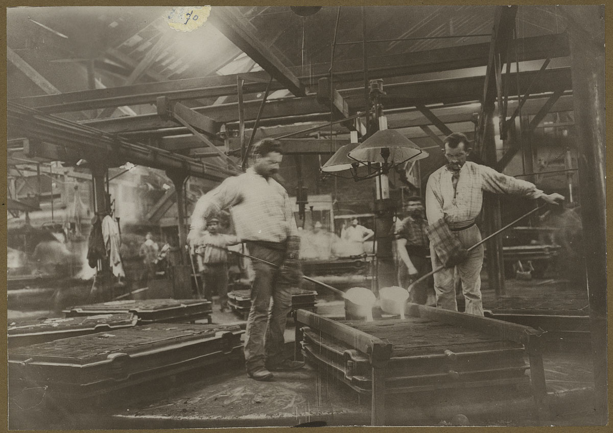 La photographie montre deux mouleurs en activité dans l'usine du Familistère.