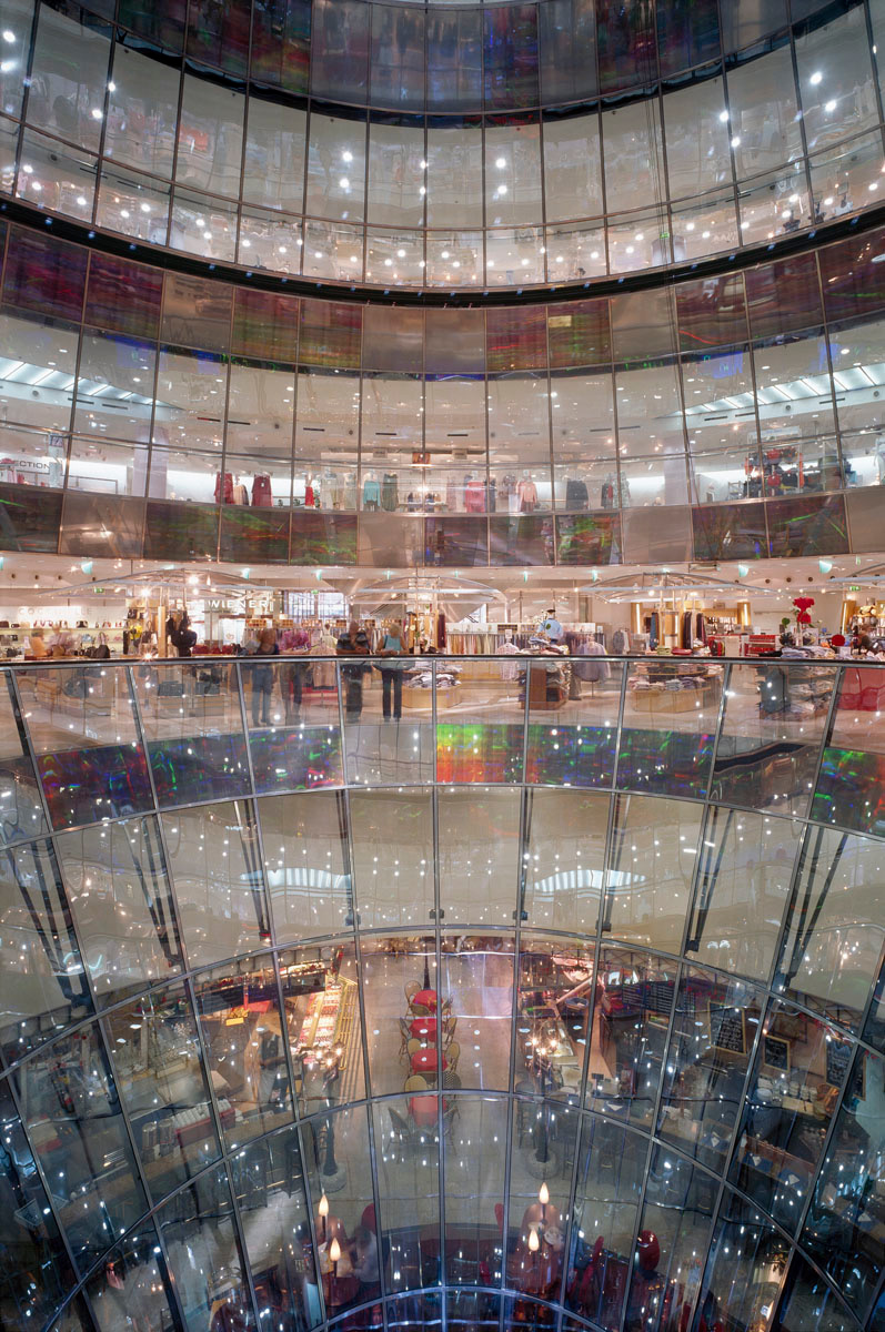 La photographie montre un centre commercial à travers une façade de verre.
