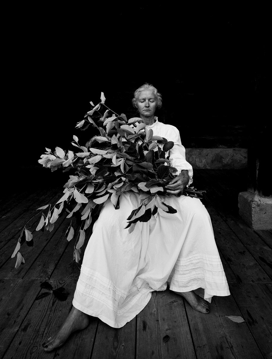 La photographie montre une femme assise en robe blanche, un bouquet de feuilles 