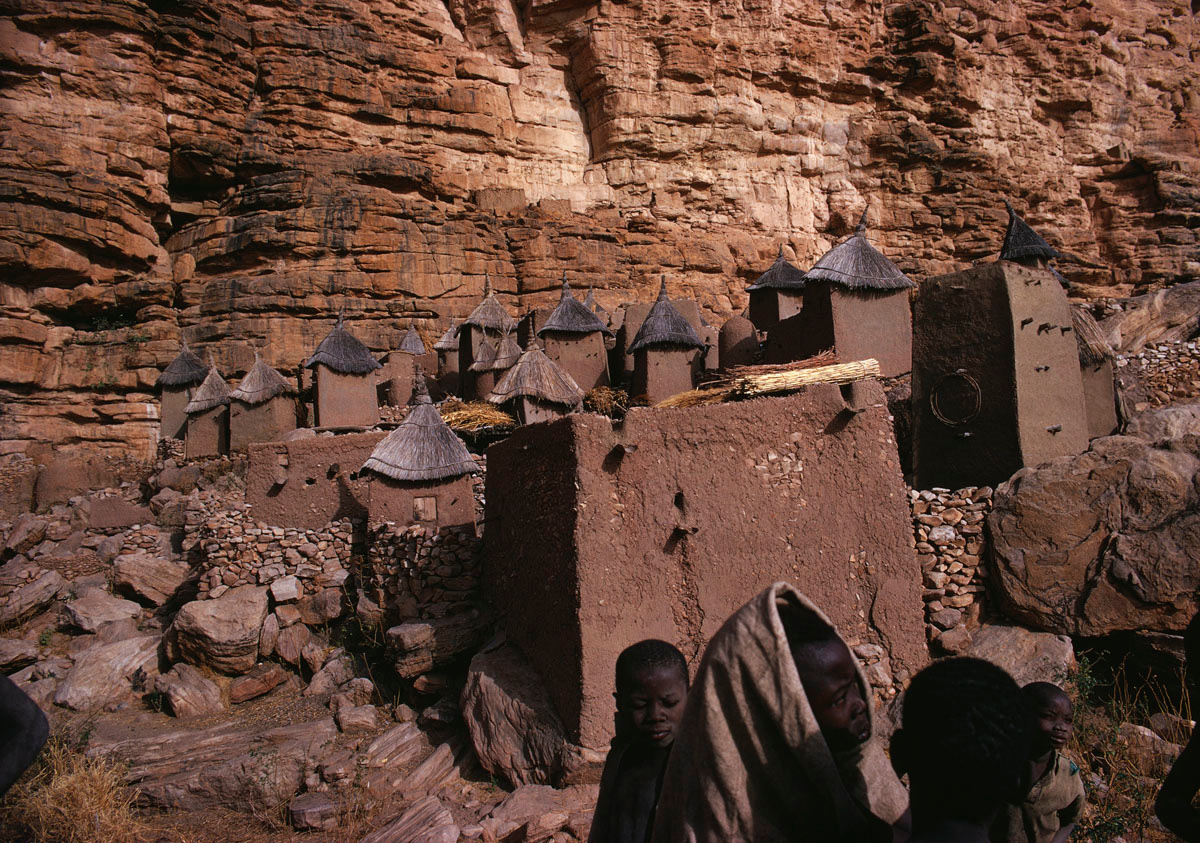 La photographie montre un village de maisons en terre au pied d'(une falaise.