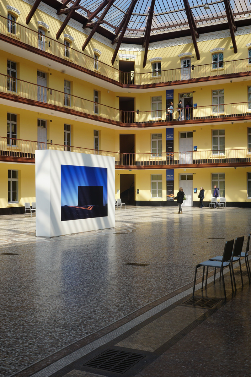 La photographier montre une cimaise installée dans une cour ensoleillée.