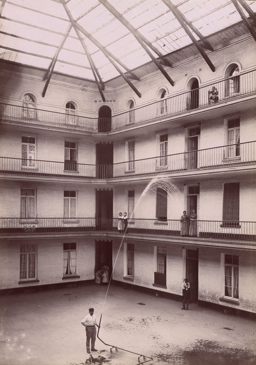 La photographie montre la cour de l'aile gauche du Familistère en cours d'arrosa