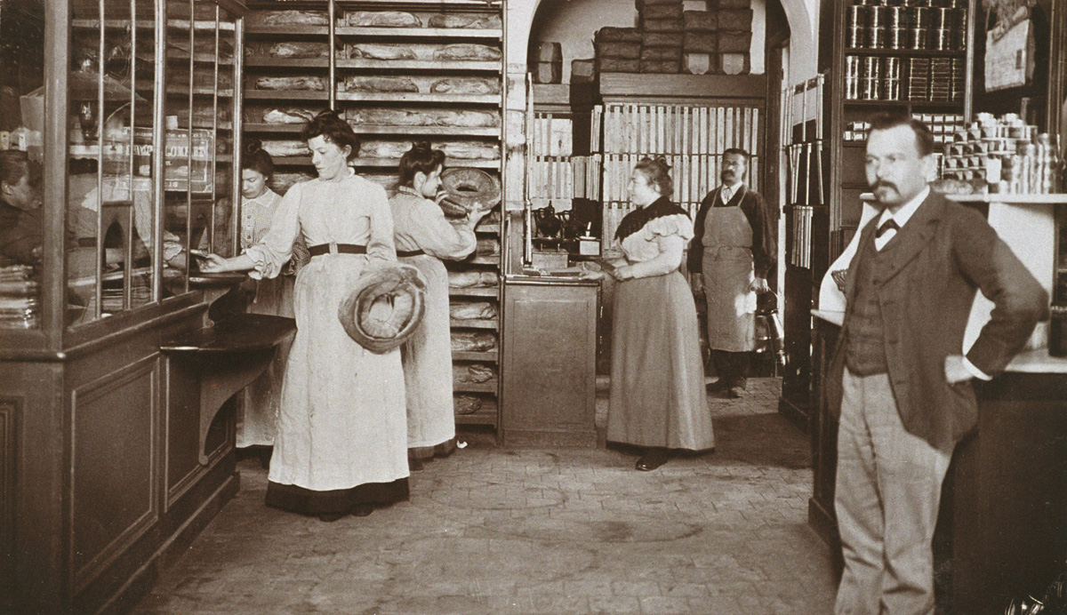 La photographie met en scène vendeurs et clientes dans l'épicerie.