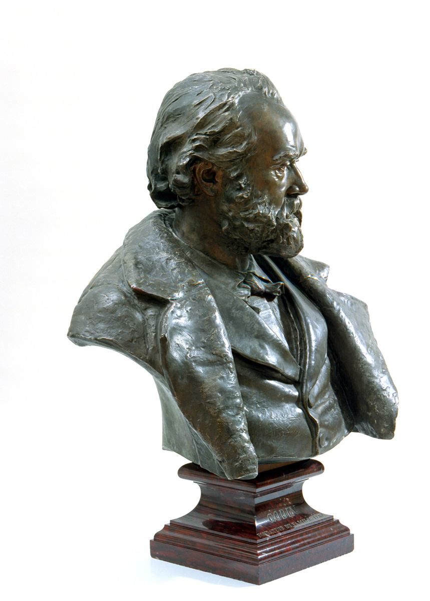 Le portrait en bronze montre Godin en buste, regardant vers la droite.