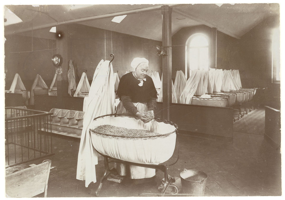 La photographie montre Madame Roger préparant le matelas d'un berceau.