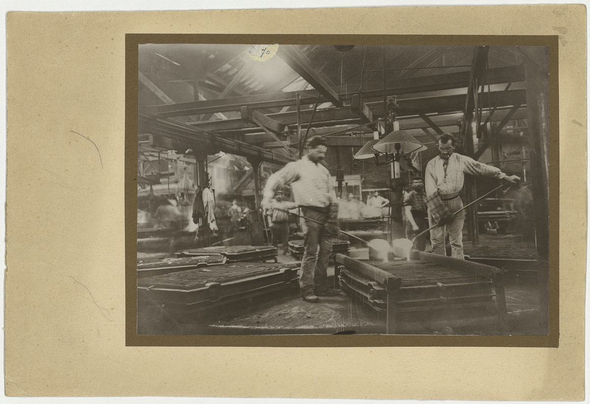 La photographie montre deux mouleurs en activité dans l'usine du Familistère.