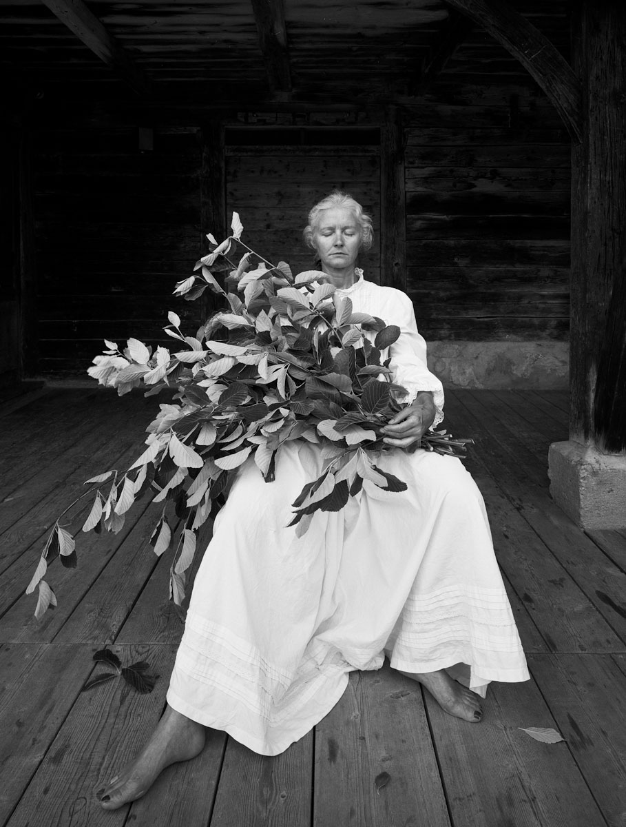 La photographie montre une femme assise en robe blanche avec un bouquet de feuil
