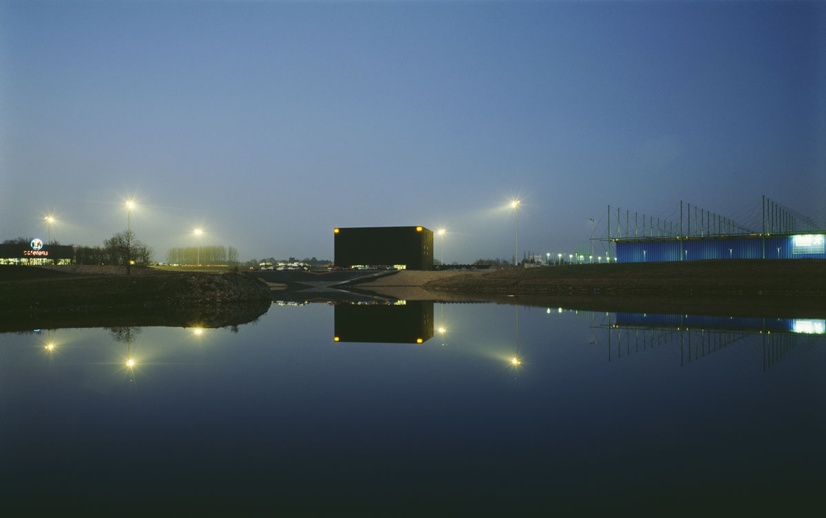 La photographie montre un bâtiment cubique à la tombée du jour.