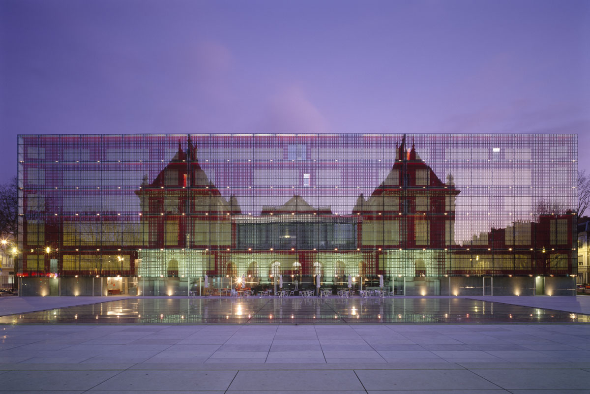 La photographie montre le reflet d'un édifice sur une façade de verre.