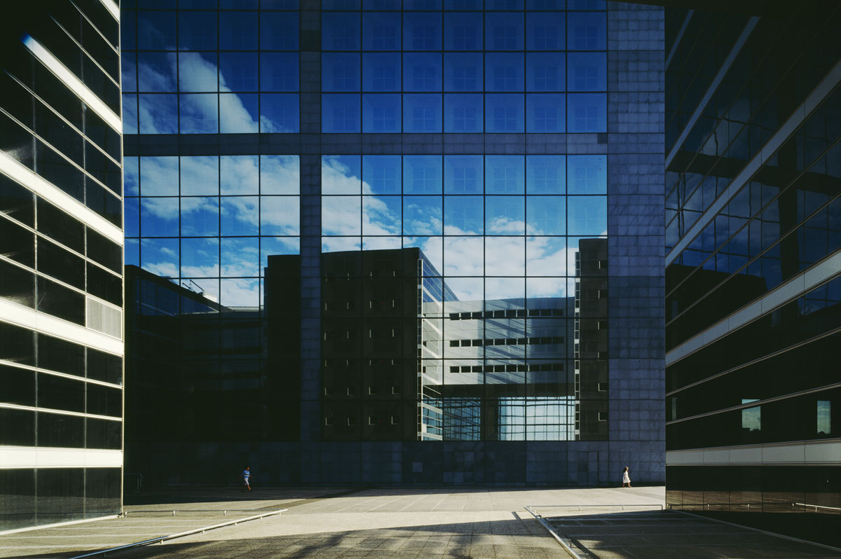 La photographie montre le reflet d'un édifice sur une façade de verre.