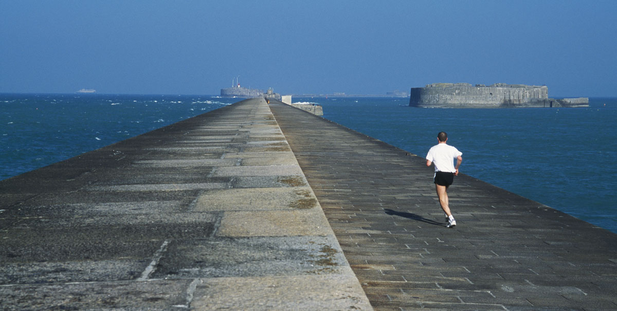 La photographie montre un homme courant en direction de la mer sur une jetée.