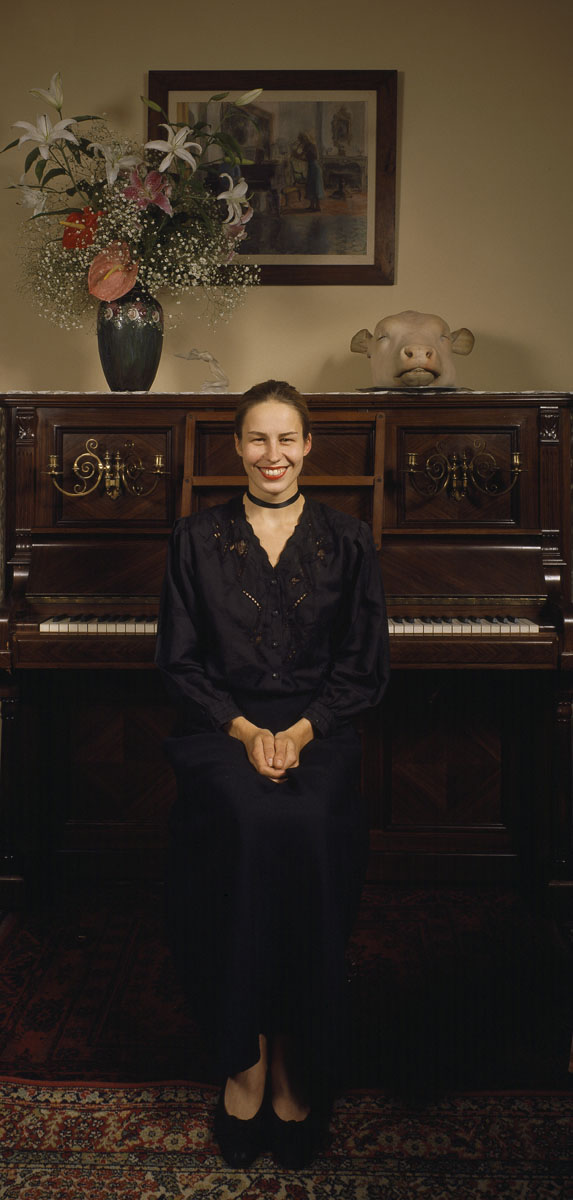 La photographie montre une jeune femme souriante assise dos à un piano