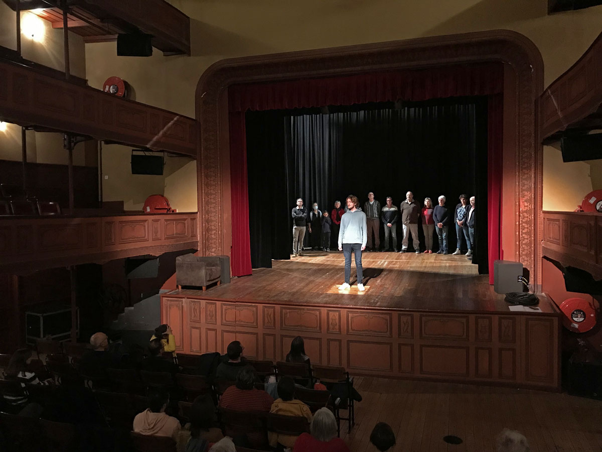 Un homme s'avance seul sur le devant de la scène du théâtre du Familistère